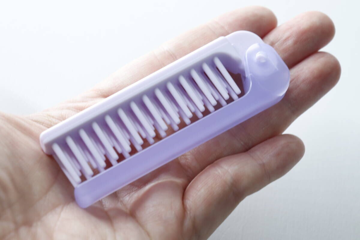 手のひらに乗せられた紫色の折りたたみ式ヘアブラシ