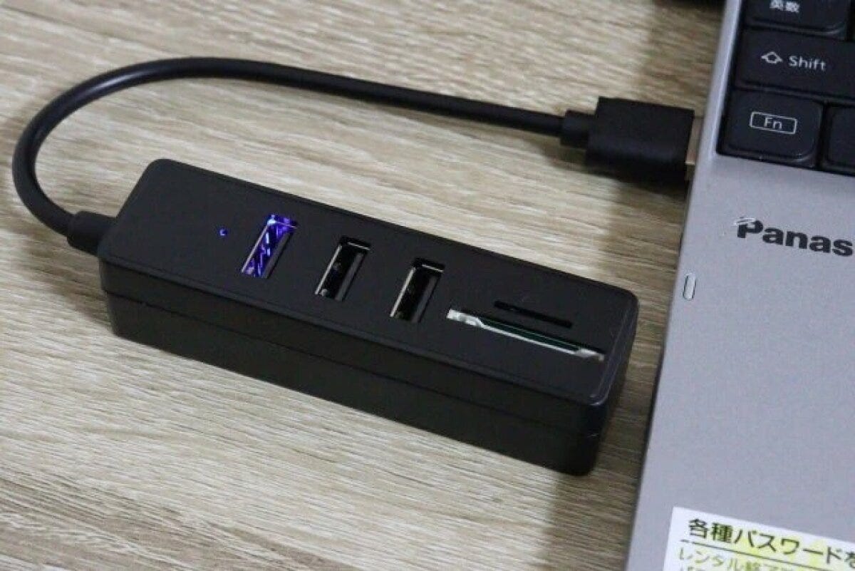 黒いUSBハブがノートパソコンに接続され、青いランプが点灯している