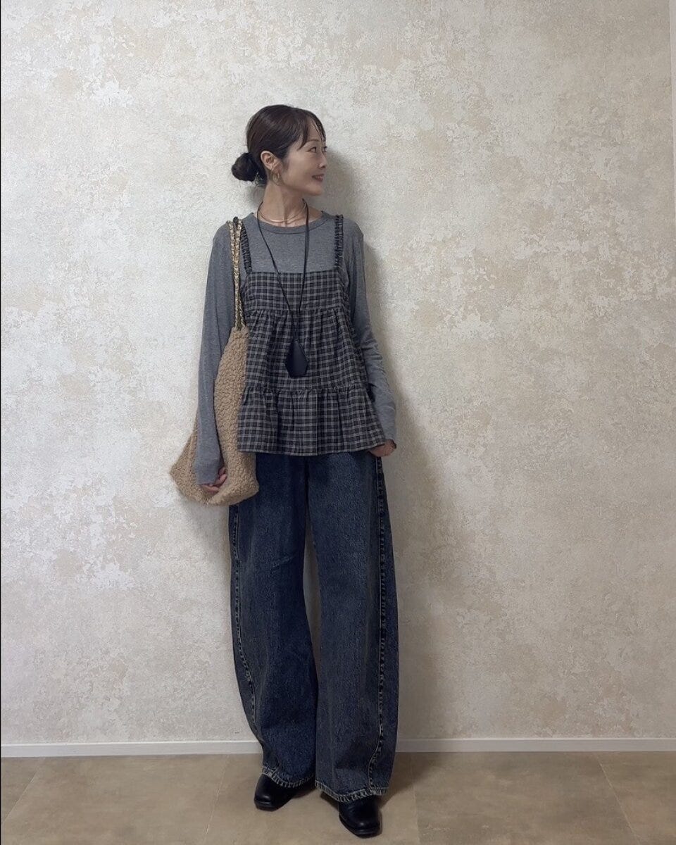 グレーのロンTとデニムにチェックキャミを重ね着した女性が横を向いて立っている
