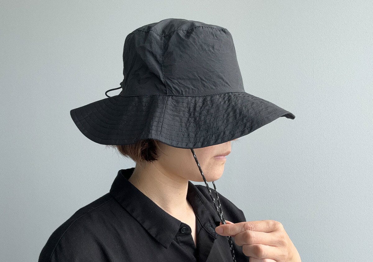 黒いサファリハットを被った女性が、あご紐を調整している横顔