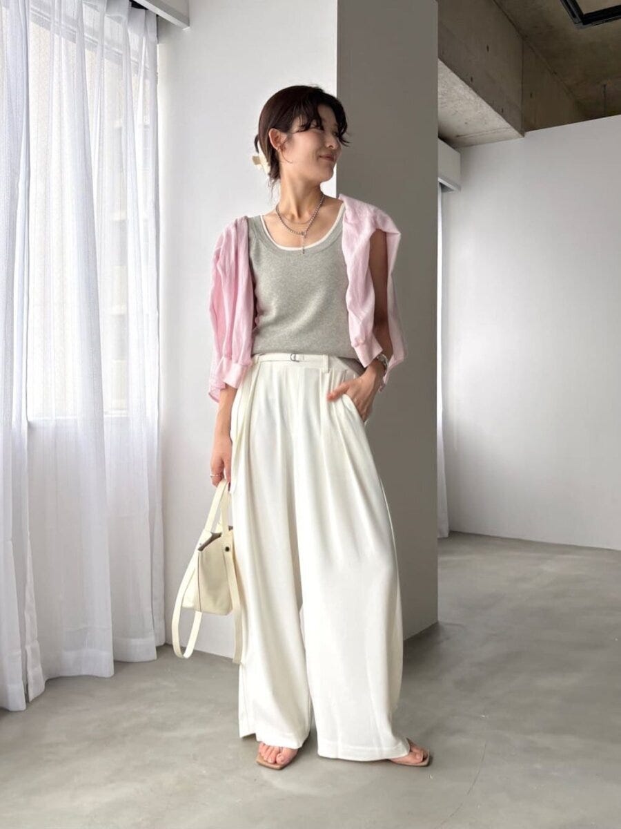 ピンクシャツを肩掛けした女性が白ワイドパンツで立つ ピンクシャツを肩掛けした女性が白ワイドパンツで立つ