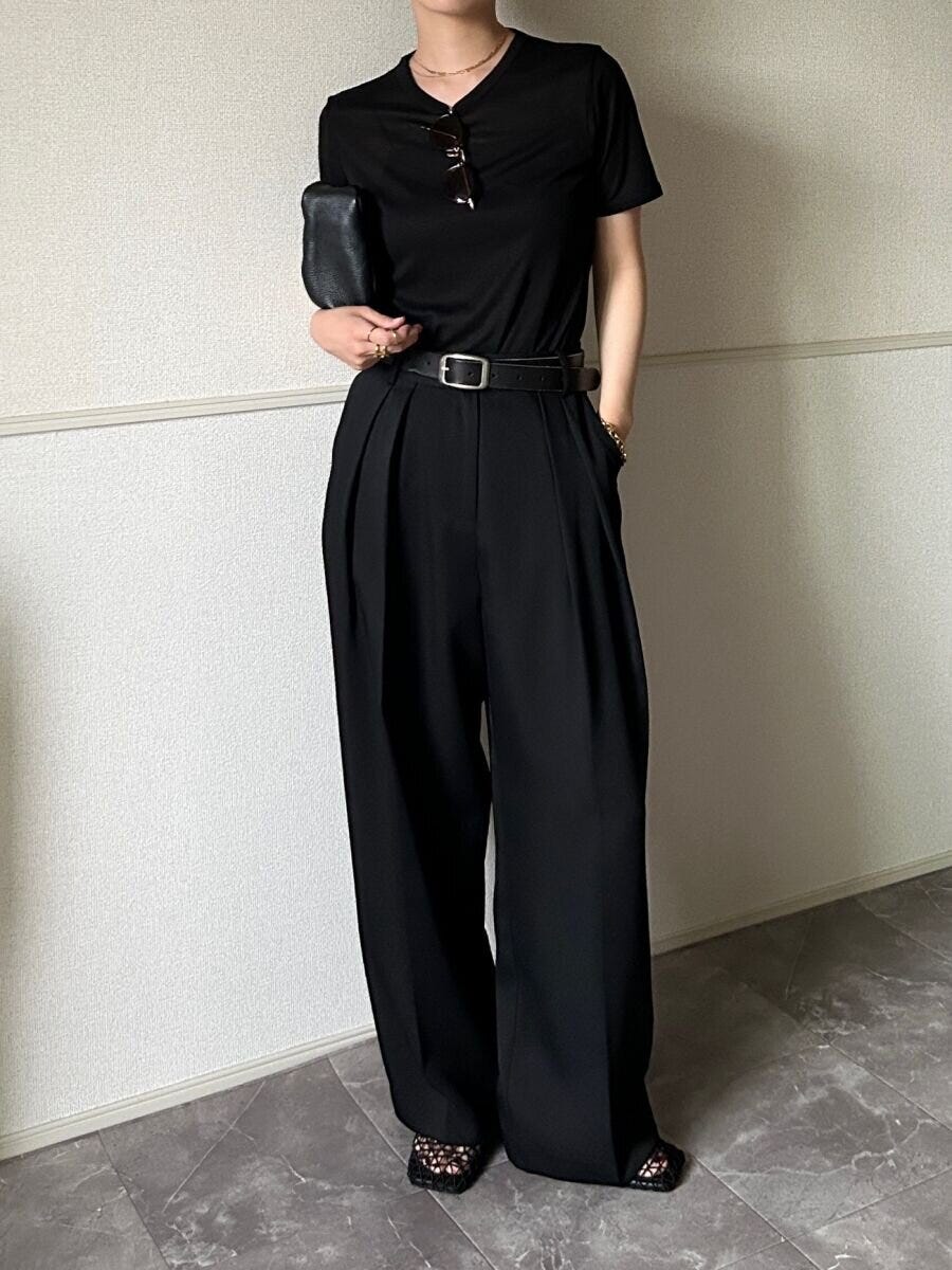 黒いシアーTシャツと黒いワイドパンツを着用し黒いベルトとクラッチバッグを持った女性が立っている