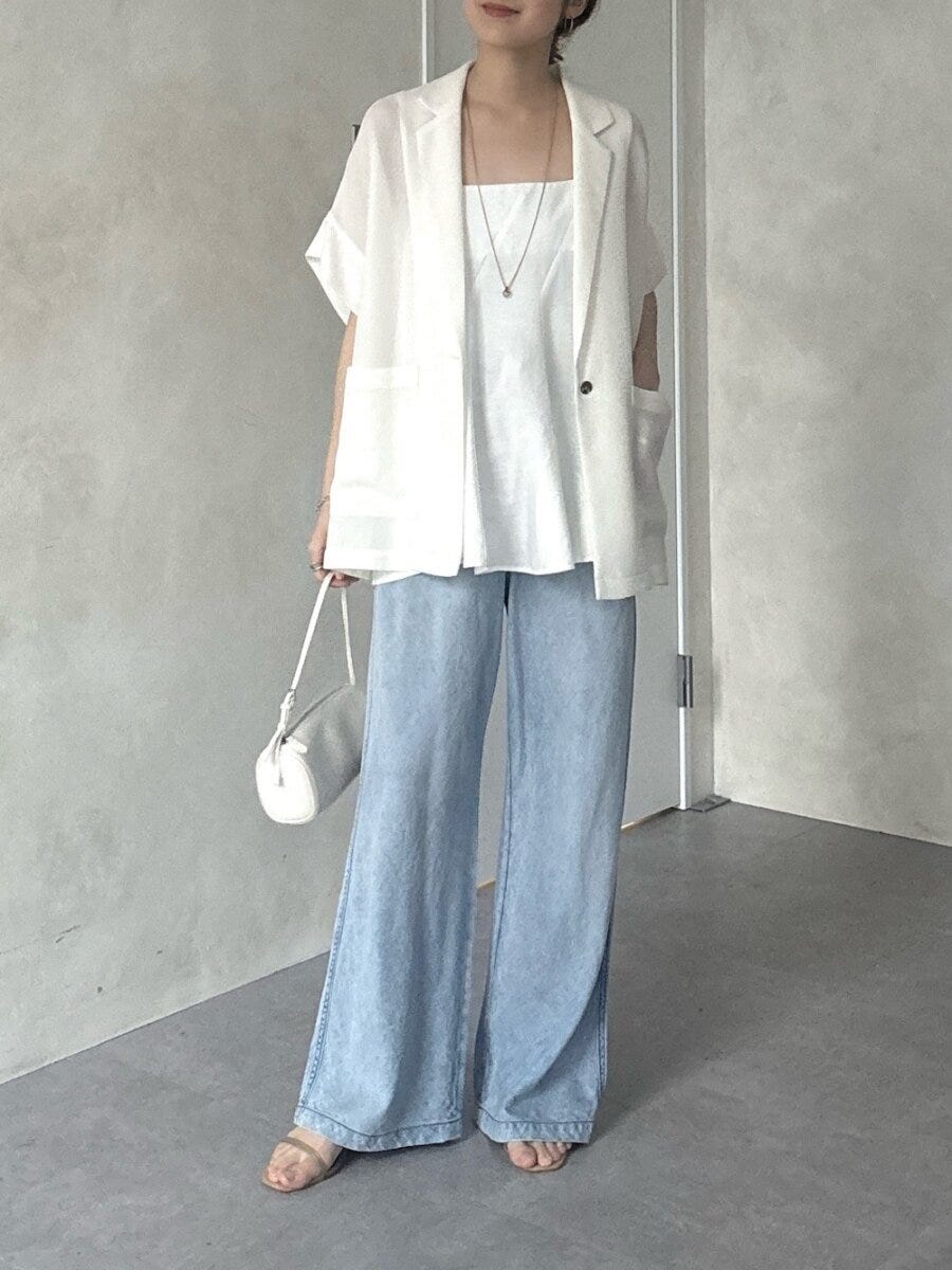 白の半袖ジャケットと水色ワイドデニムを着た女性が、白いミニバッグを持ち立っている。