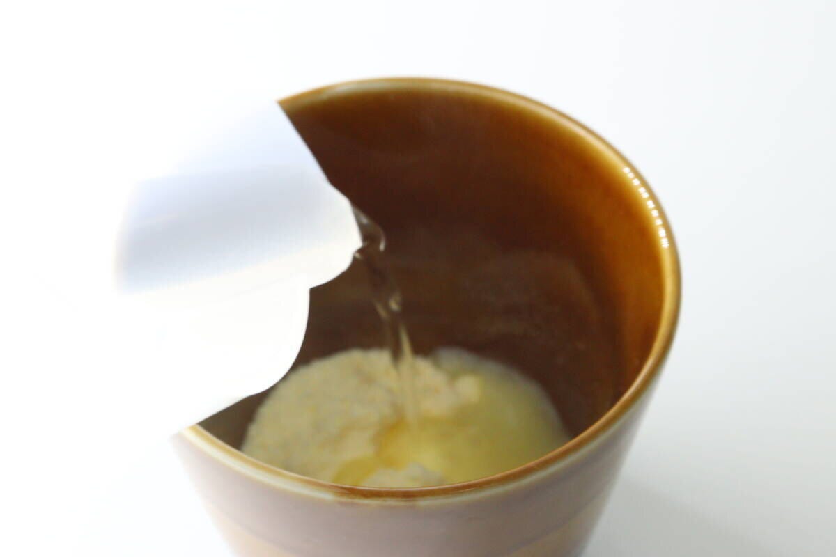 茶色のカップに入った粉末に、白い容器から熱湯を注いでいる様子
