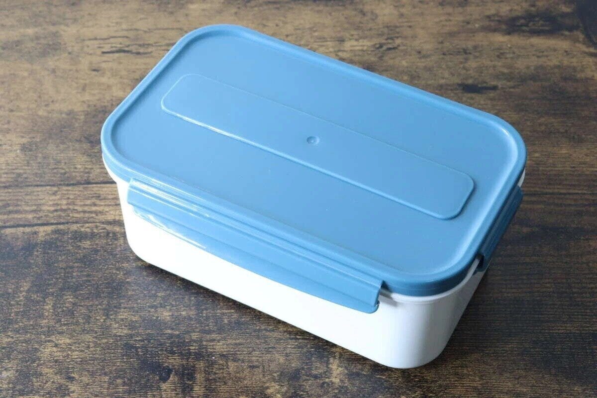 青い蓋の白い弁当箱が木目のテーブルに置かれた俯瞰写真