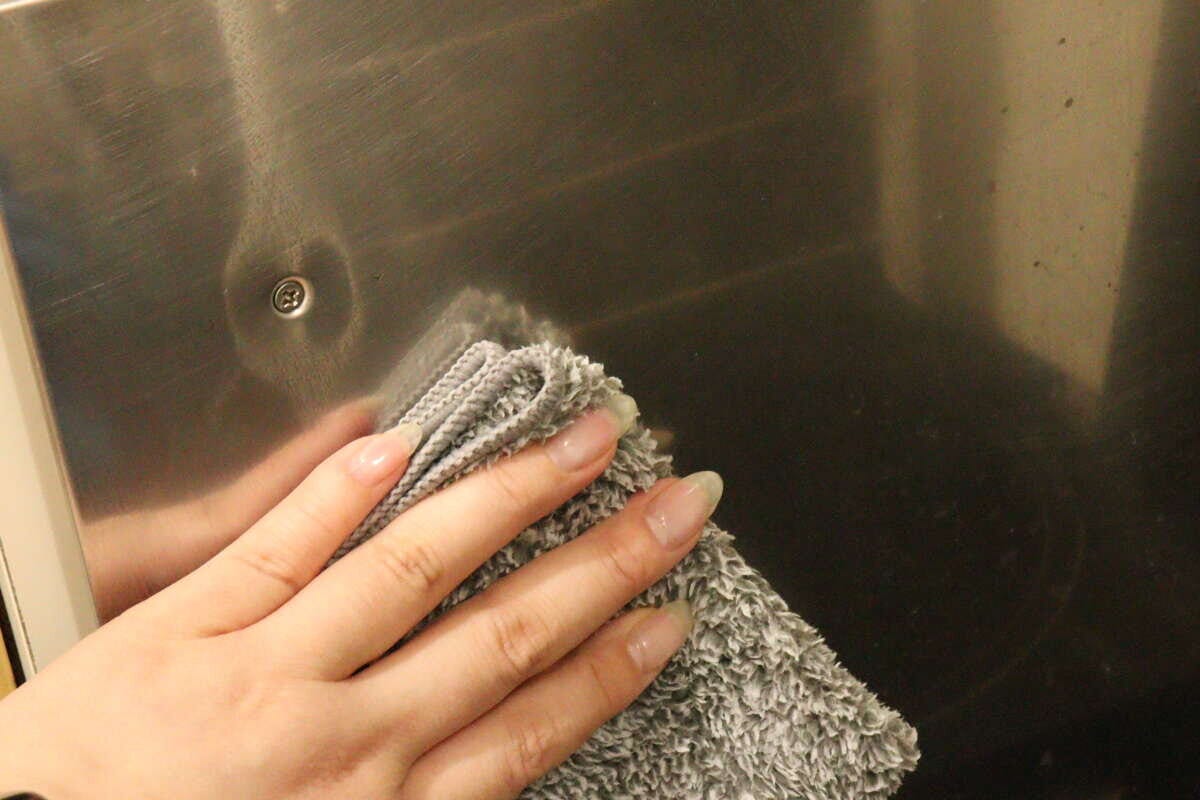 コンロのステンレス部分のしつこい汚れをふきんで擦りながら落としている様子