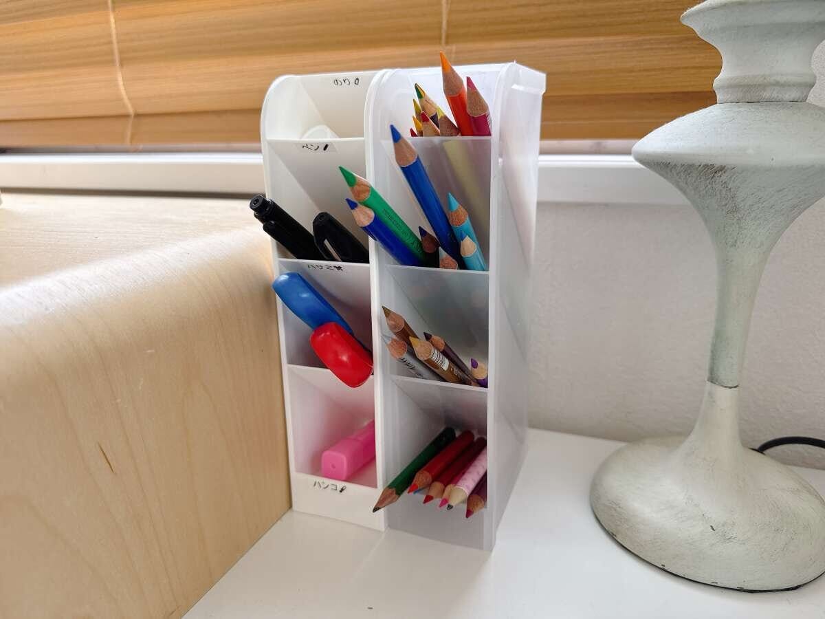 デスクの上の白い仕切りスタンドに色鉛筆やマーカー、はさみが種類ごとに収納されている