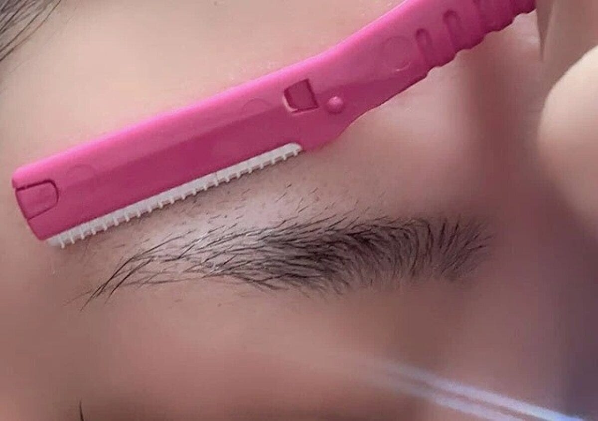 ピンク色のフェイス用カミソリで、眉毛の形を整えるように眉下の産毛を剃っている様子 ピンク色のフェイス用カミソリで、眉毛の形を整えるように眉下の産毛を剃っている様子