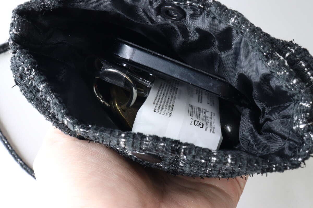 黒いツイードショルダーバッグの中にスマホや鍵などの荷物が入っている様子を上から覗き込んでいる