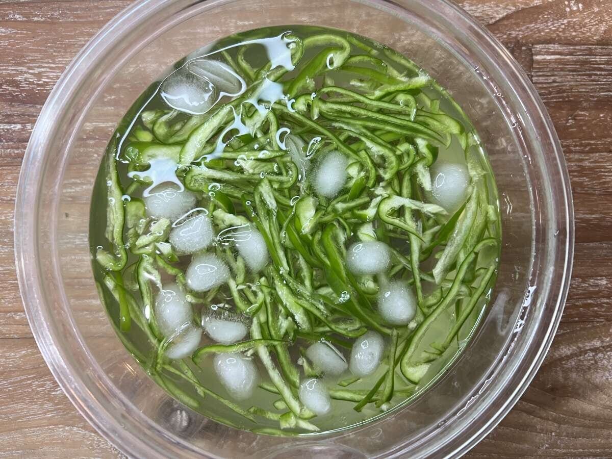 千切りピーマンが氷と水が入った透明なボウルに浸されている