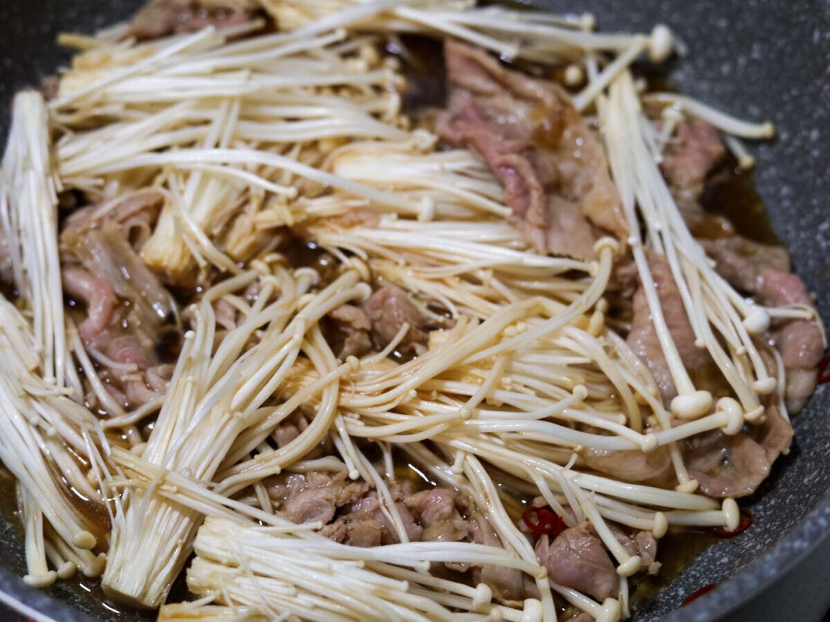 豚肉と煮汁の入ったフライパンにえのきが加えられた状態 豚肉と煮汁の入ったフライパンにえのきが加えられた状態
