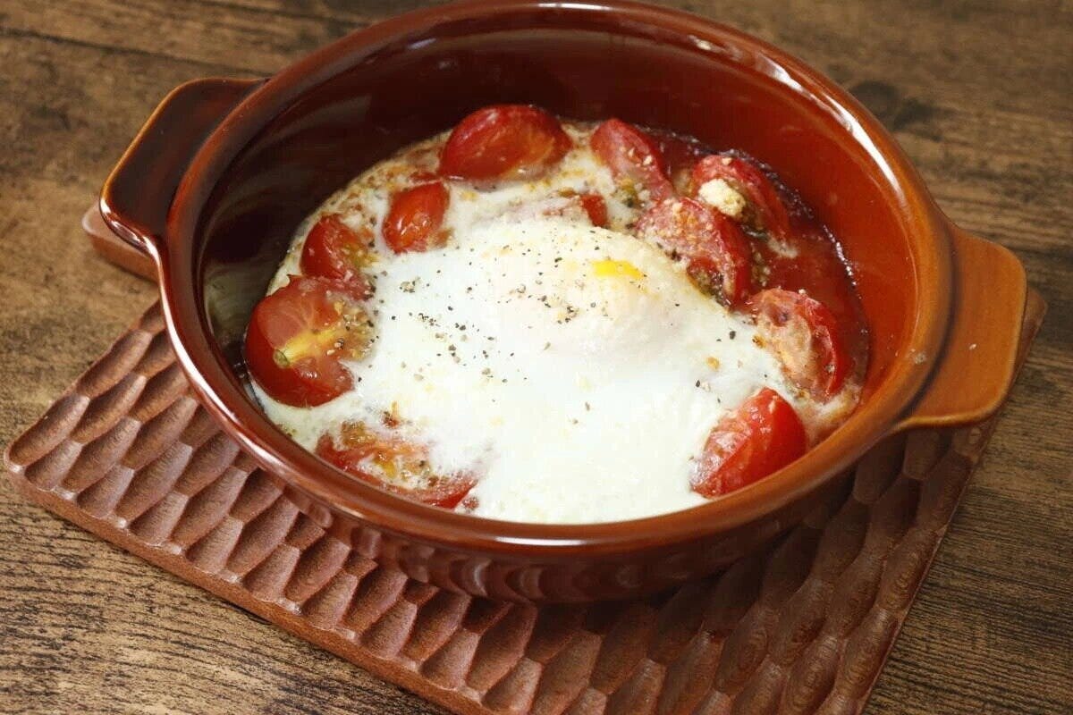 茶色のグラタン皿にミニトマトと卵のオーブン焼きが完成し、食卓に置かれている