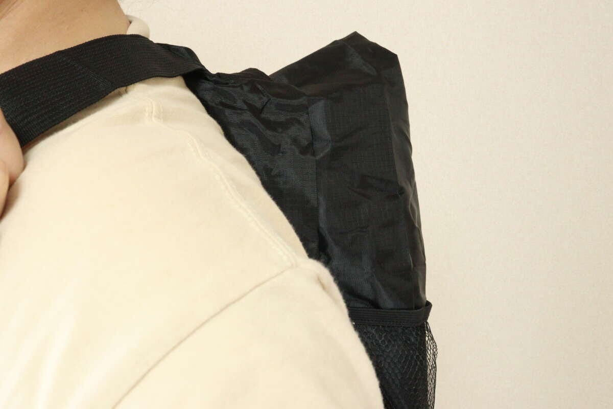ベージュのシャツを着た人物が、黒いトート型バックパックをバックパックとして背負っている後ろ姿。