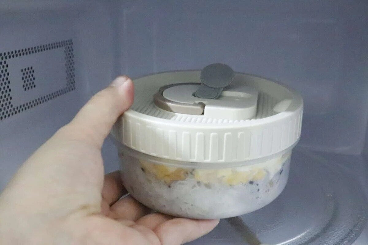 電子レンジ内で丸い弁当箱のエア弁を開ける手元