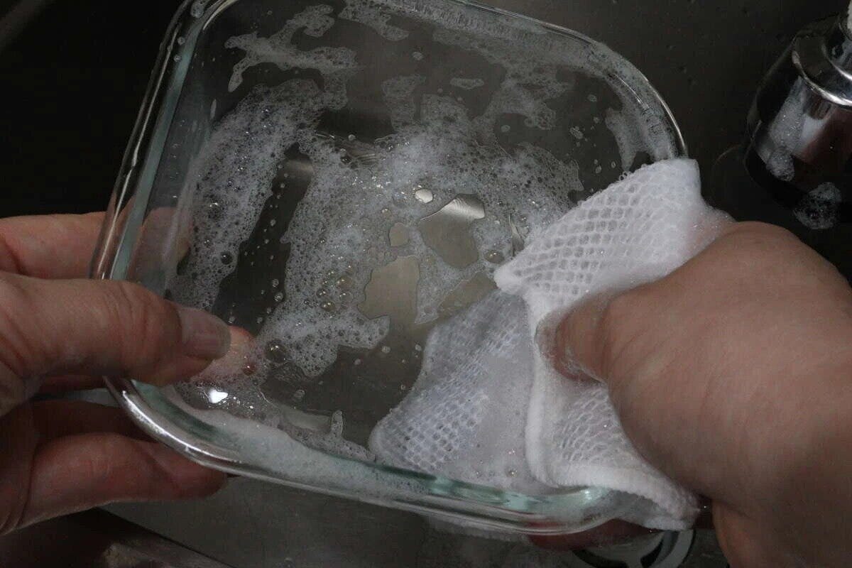 白いメッシュクロスで泡立てながらガラス容器を洗う手元