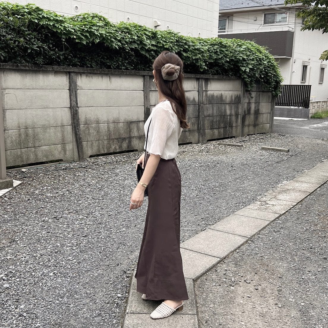 ベージュ系のバイカラーシアートップスとブラウンロングスカートを着ている女性