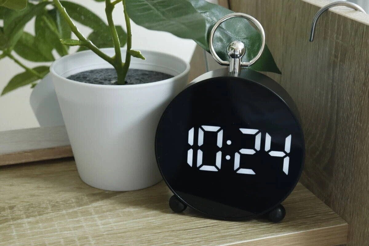 黒いLEDデジタル時計が観葉植物の隣の棚に置かれている