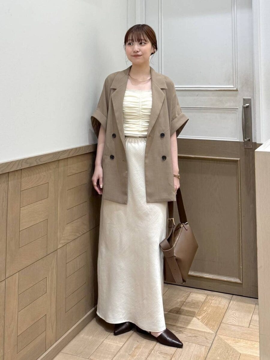 茶色ジャケットと白ナロースカートを着用し茶色バッグを持つ女性