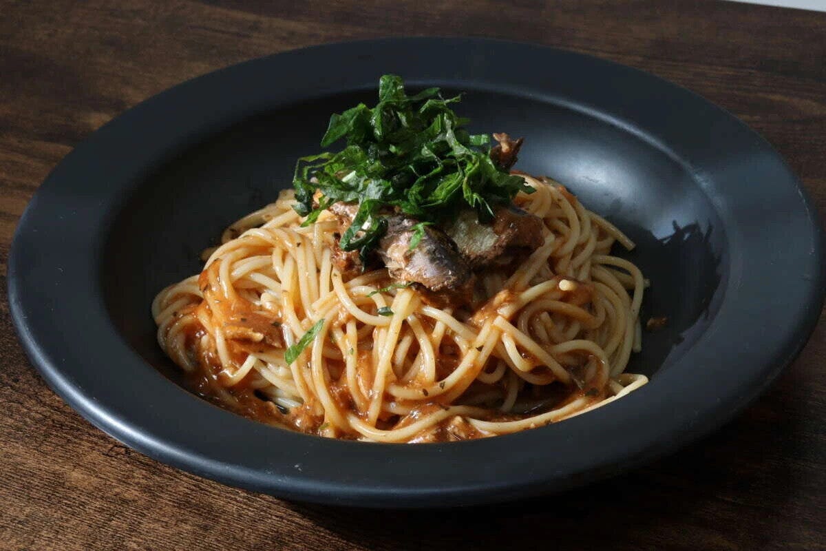 黒い皿に盛られた、大葉が乗ったいわしトマト煮パスタのアップ 黒い皿に盛られた、大葉が乗ったいわしトマト煮パスタのアップ