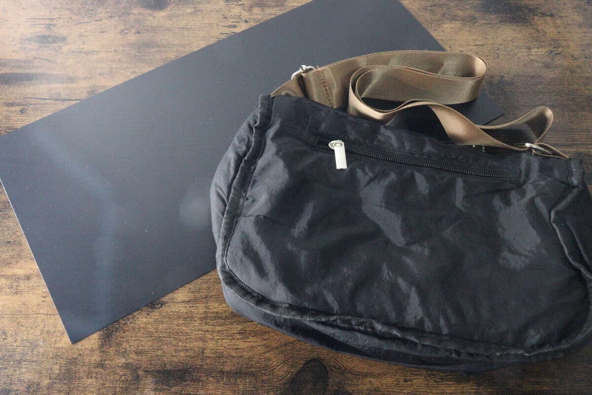 黒いプラ底板の横に置かれたくたっとした黒いショルダーバッグ 黒いプラ底板の横に置かれたくたっとした黒いショルダーバッグ