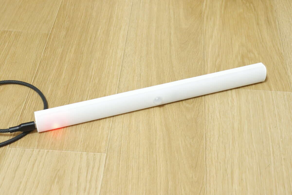 Type-Cケーブルで充電中の本体(赤色LED点灯) 木目の床に置いた本体にType-Cケーブルをつないで充電している写真。端の赤いLEDが点灯している