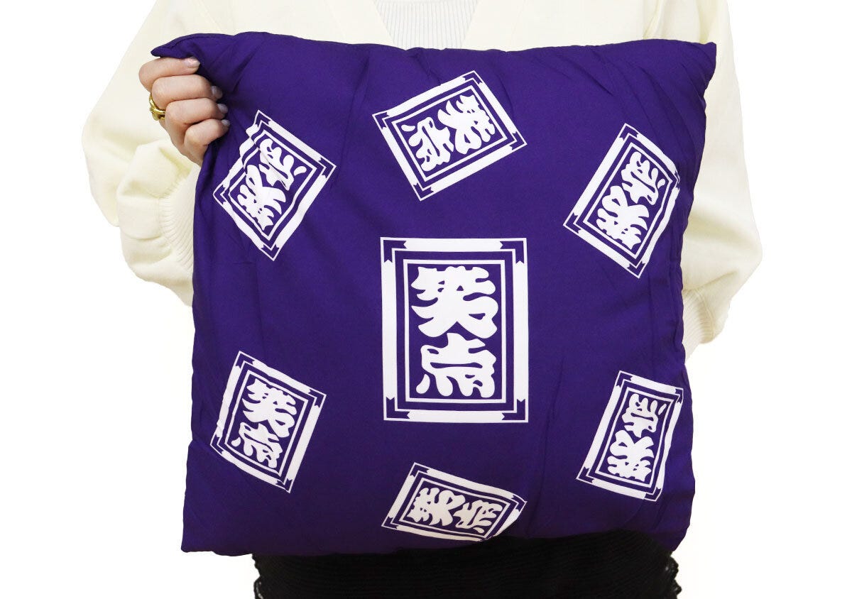 白いニットの女性が笑点座布団クッションを抱きかかえている様子