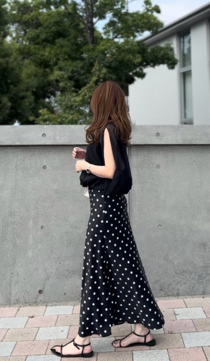 黒いトップスとドット柄マーメイドスカートを着用し、横向きで歩く女性 黒いトップスとドット柄マーメイドスカートを着用し、横向きで歩く女性