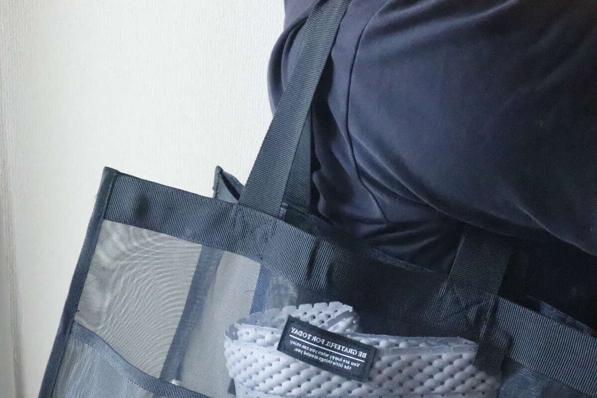 黒いメッシュバッグを肩に掛けている人の上半身、バッグの中身が少し見える 黒いメッシュバッグを肩に掛けている人の上半身、バッグの中身が少し見える