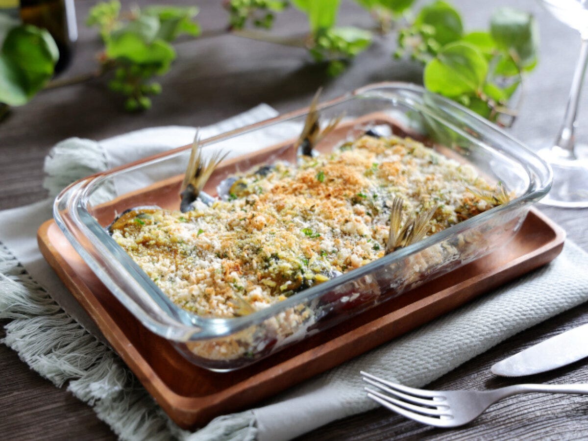 木製のトレイに乗ったガラス製の耐熱皿に入った、焼き上がったいわしとトマトのパン粉焼き 木製のトレイに乗ったガラス製の耐熱皿に入った、焼き上がったいわしとトマトのパン粉焼き