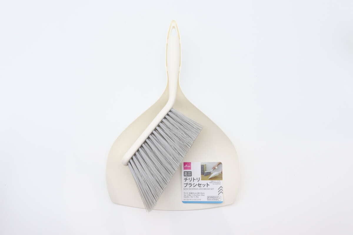 白い背景に、ベージュ色のミニチリトリとブラシが重なって置かれている。チリトリには商品ラベルが見える。 白い背景に、ベージュ色のミニチリトリとブラシが重なって置かれている。チリトリには商品ラベルが見える。