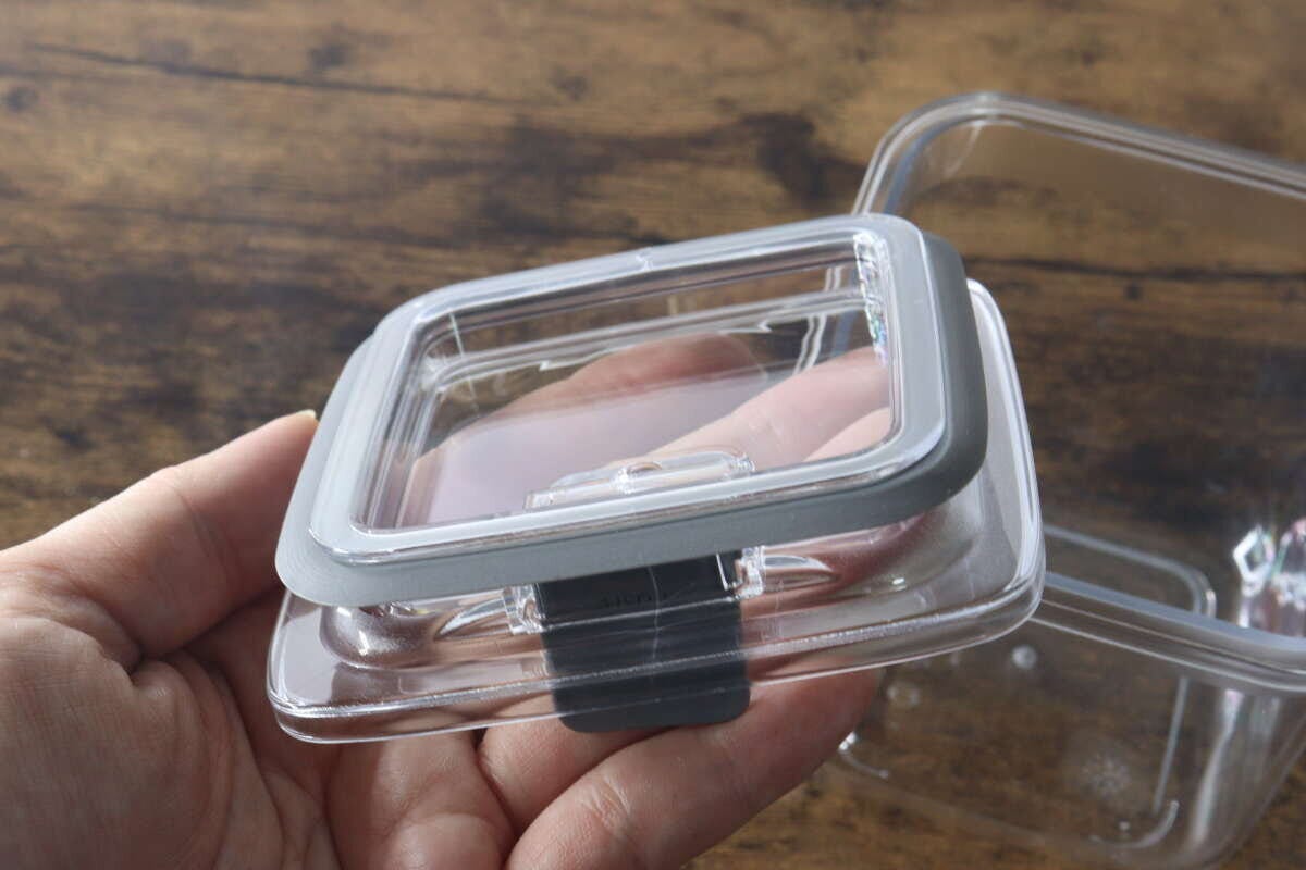 女性の手が密閉容器のフタを裏返しに持ち、グレーのパッキンが付いているのが見える 女性の手が密閉容器のフタを裏返しに持ち、グレーのパッキンが付いているのが見える