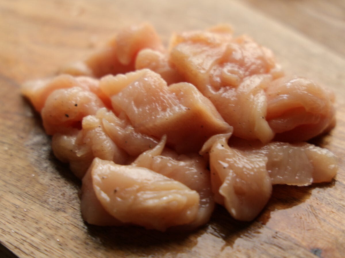 下味をつけられた鶏むね肉のそぎ切りが木製のまな板に山状に盛られている様子 下味をつけられた鶏むね肉のそぎ切りが木製のまな板に山状に盛られている様子