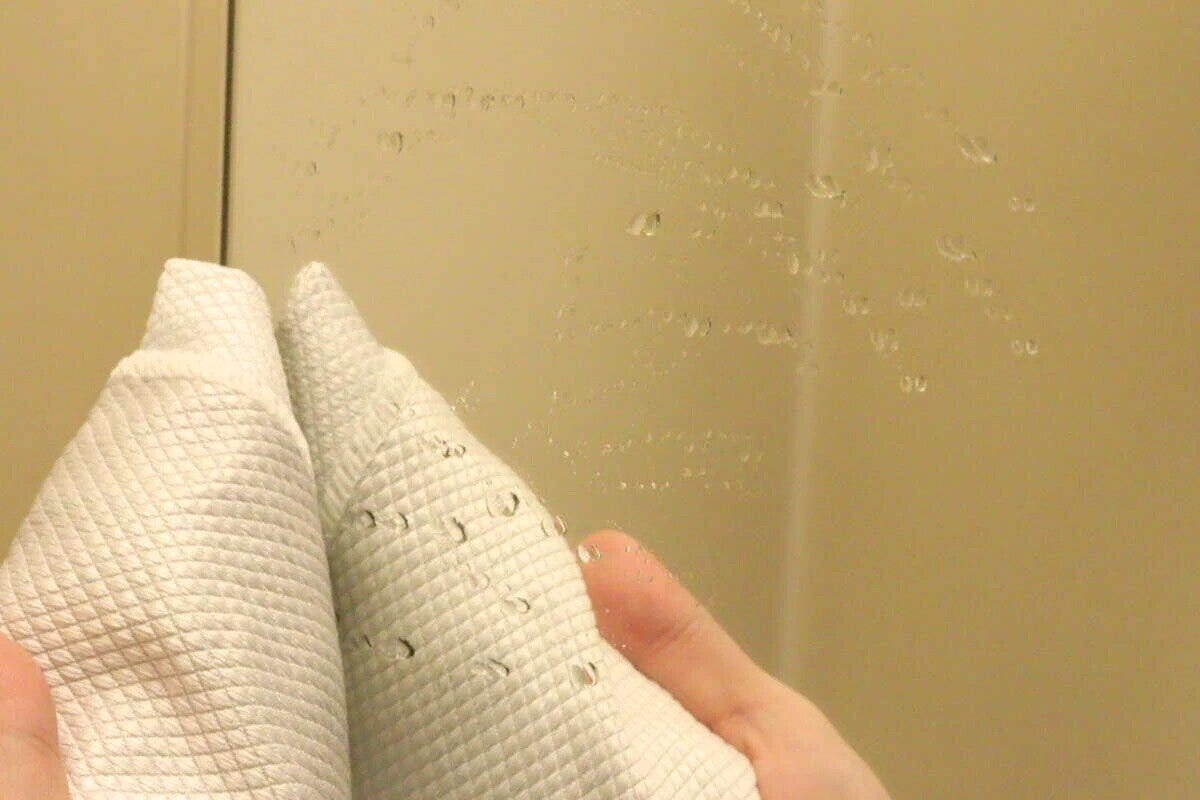 水滴のついた鏡を白いクロスで拭いている手元 水滴のついた鏡を白いクロスで拭いている手元