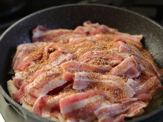 豚バラ肉は、食べやすい大きさに切り、広げて上に置いたら、顆粒コンソメと黒こしょうをまんべんなく振りかける。