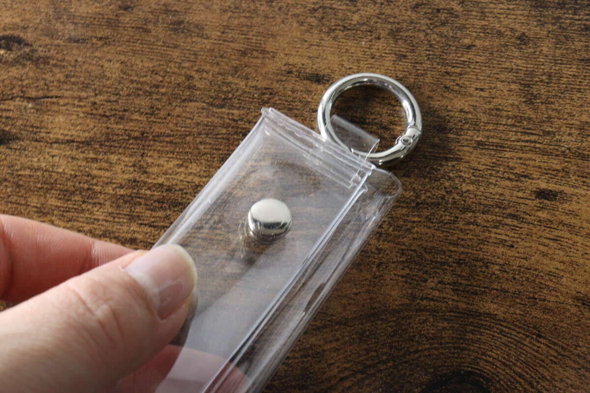 手がPVCコインポーチの留め具部分をつまんで開けようとしている