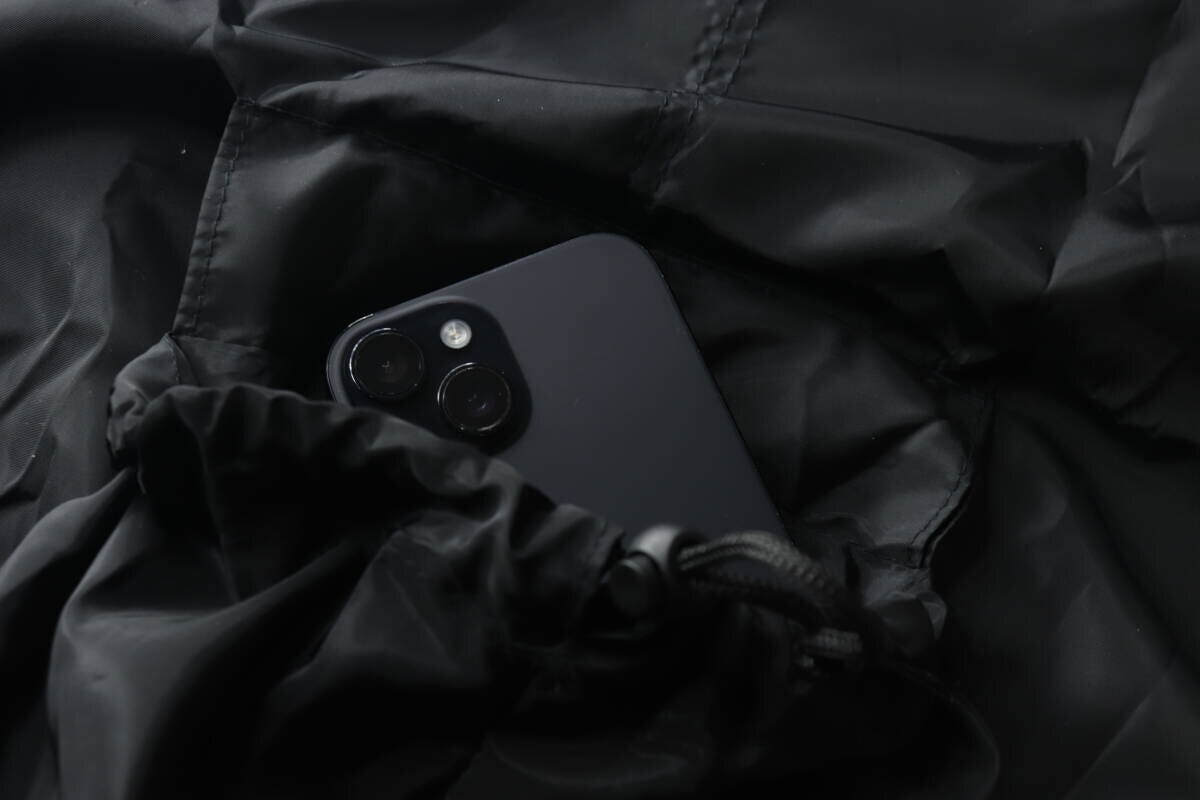 ナップサックのポケット部分に黒いスマートフォンが入っている