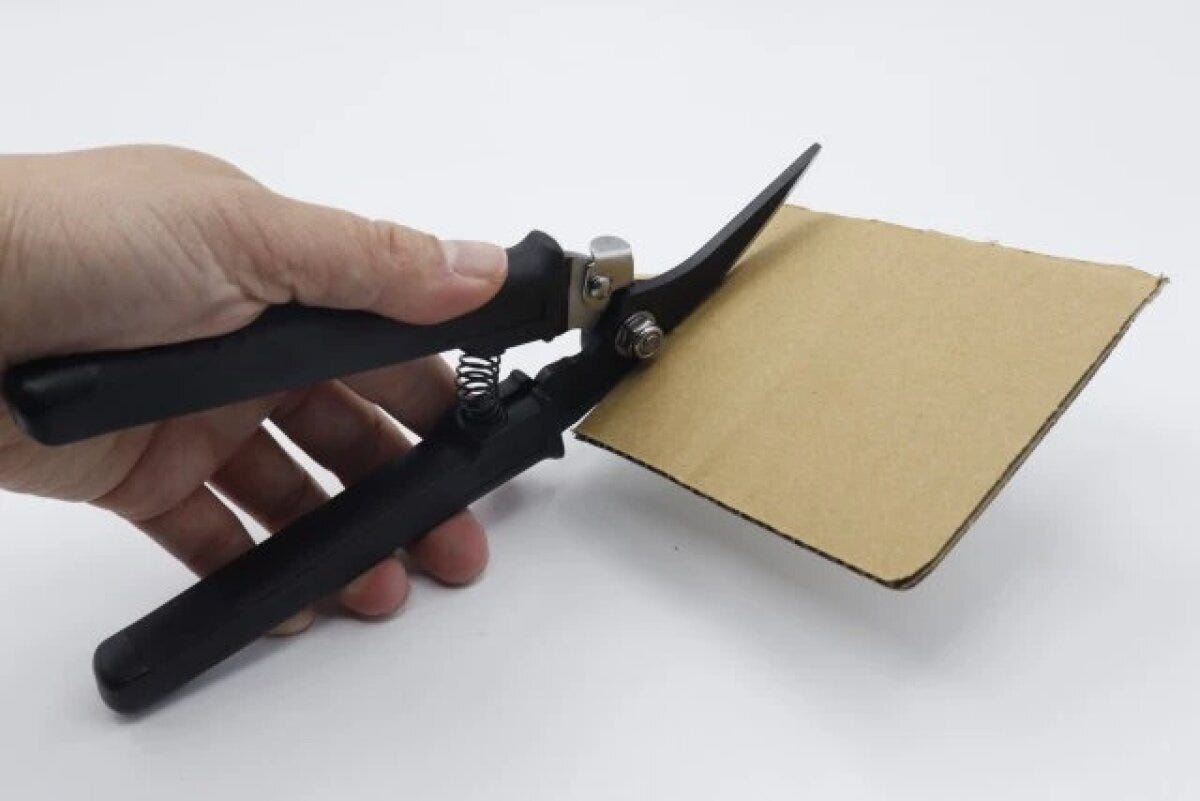 手が黒い万能ハサミで厚手の段ボールを切っている