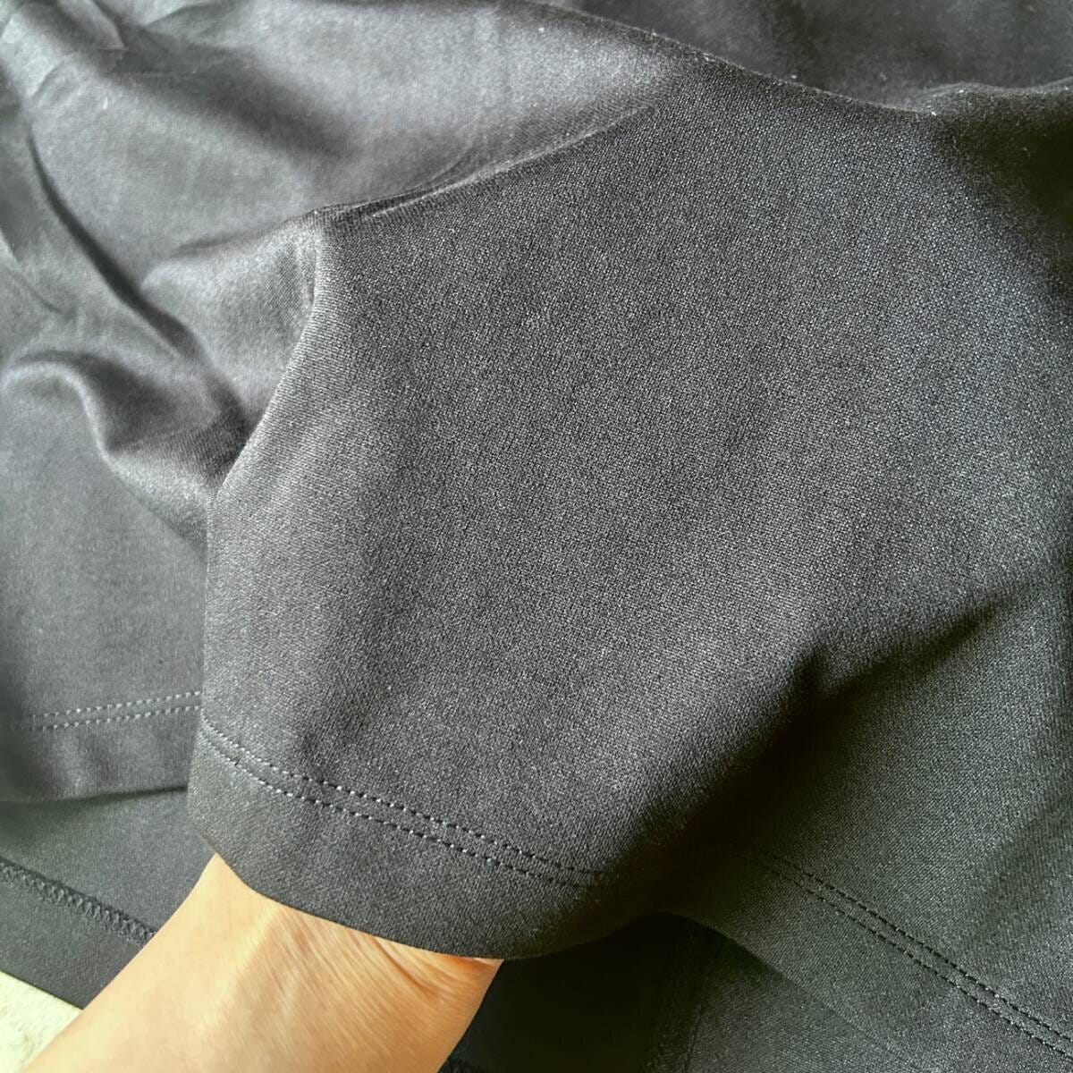 黒いTシャツの生地を指でつまんでおり、素材の質感がわかるアップ