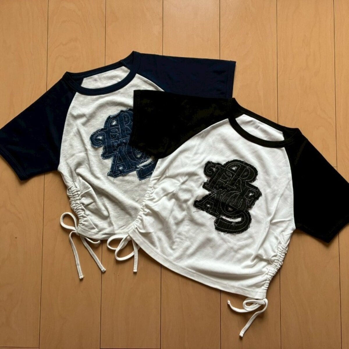 黒と白のラグランTシャツが木床に並べられ裾にリボンが見える