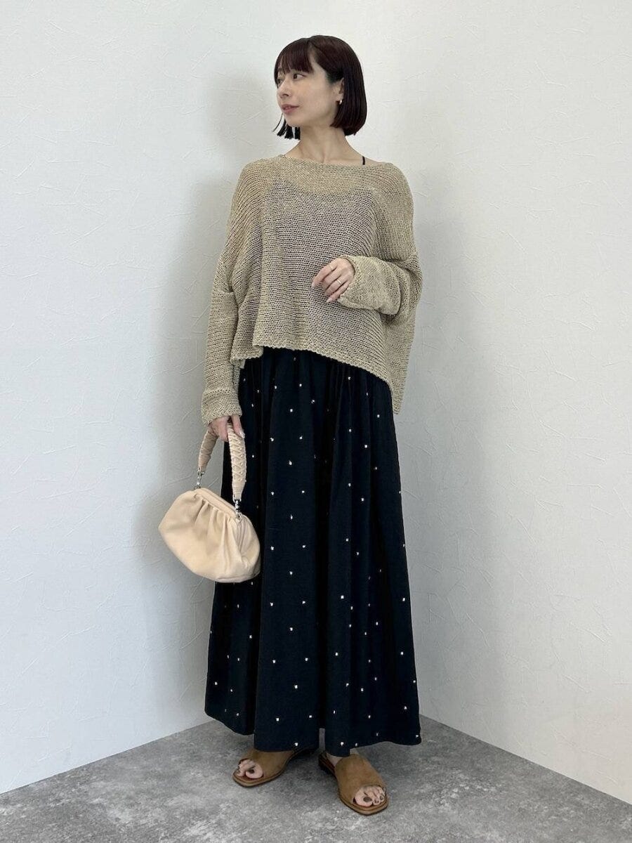 黒ドットワンピにベージュメッシュニットを重ねミニバッグを持つ女性
