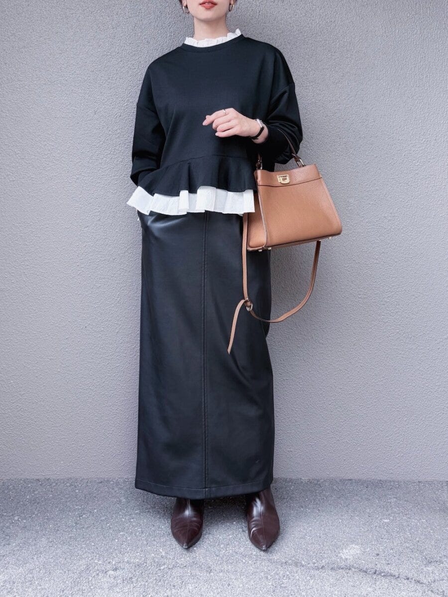 黒スウェットとレザーロングスカートの女性がバッグを持つ