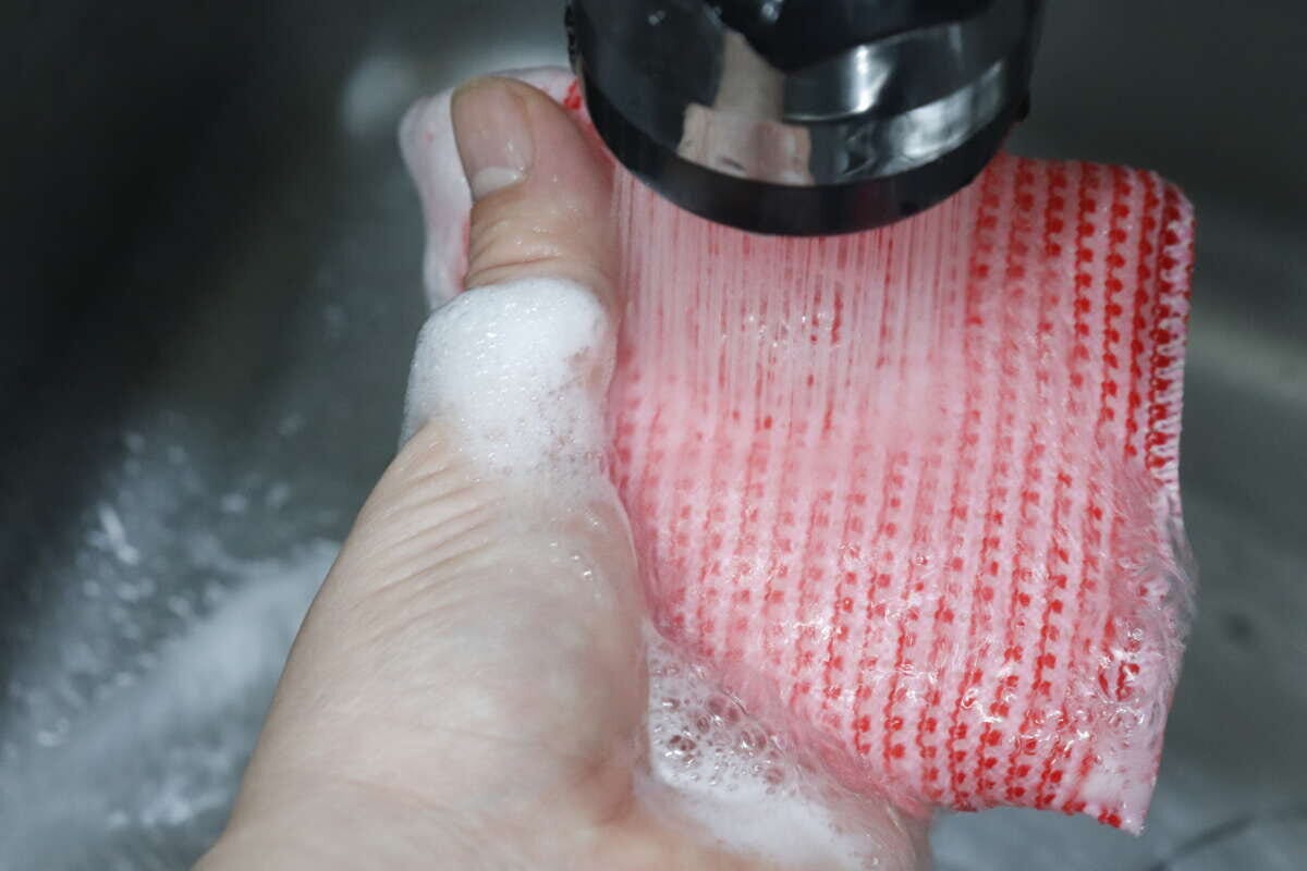 蛇口から流れる水で泡を洗い流している赤いスポンジ 蛇口から流れる水で泡を洗い流している赤いスポンジ