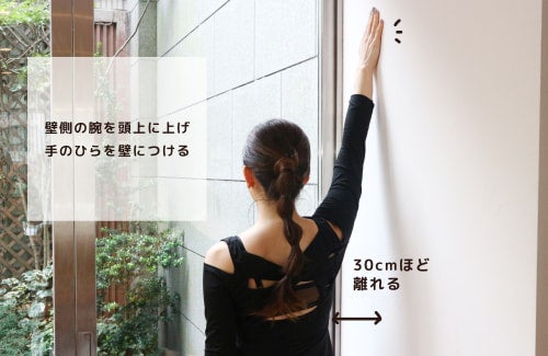 壁側の腕を頭上に上げ手のひらを壁につける