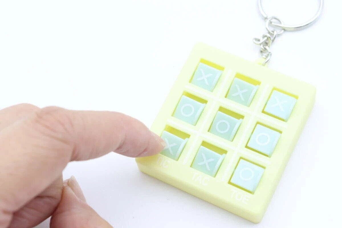 黄色いマルバツゲームキーホルダーの盤面を指で操作している手元 黄色いマルバツゲームキーホルダーの盤面を指で操作している手元