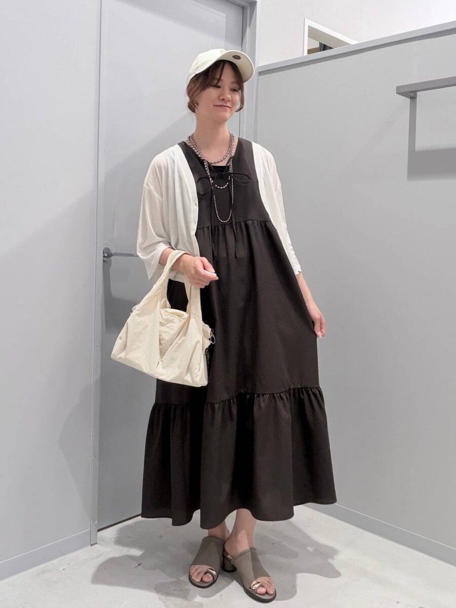 白いカーディガンと黒ワンピースの女性がバッグを持ち笑顔