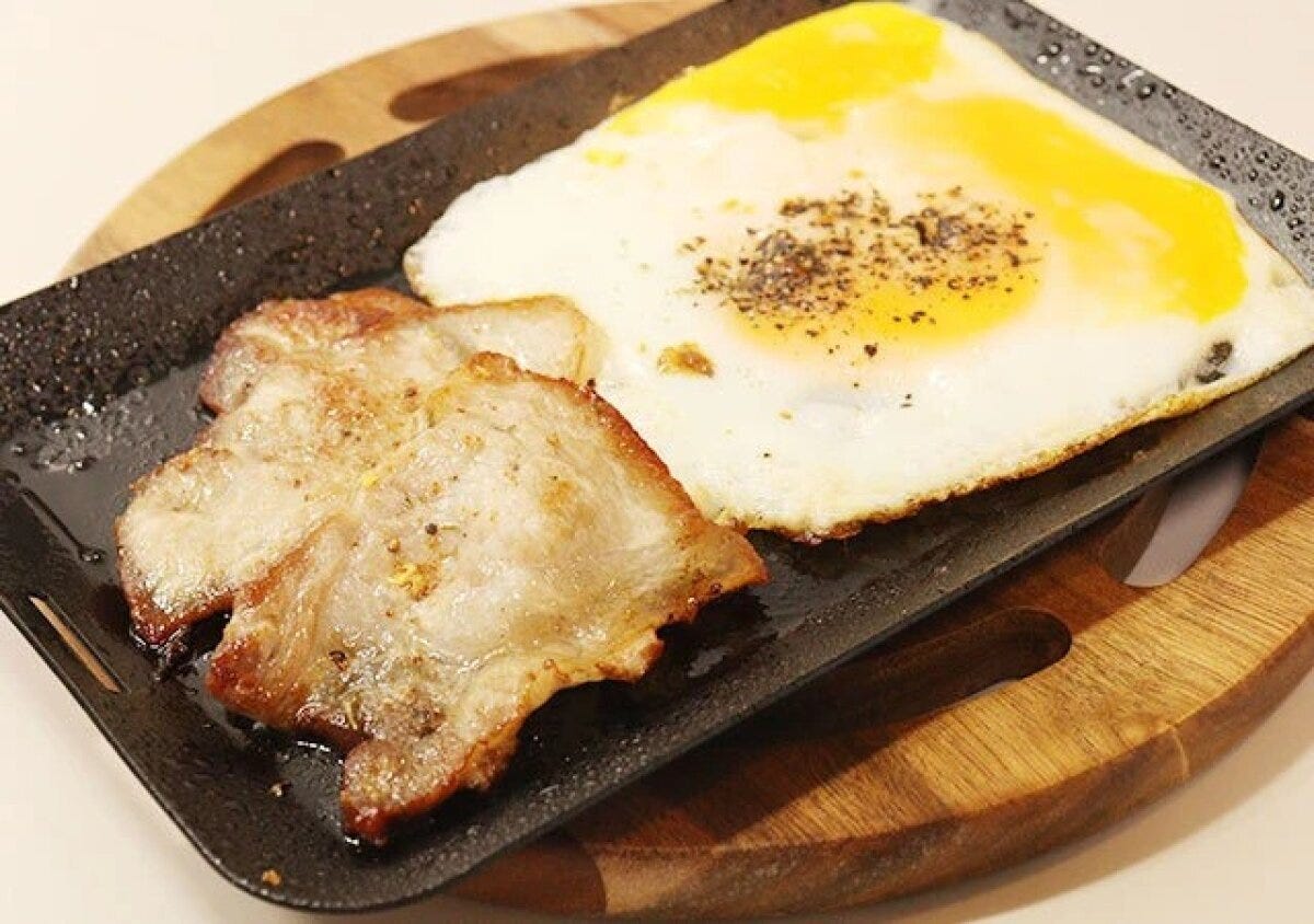 黒いグリルプレートに乗った目玉焼きと豚肉のソテー