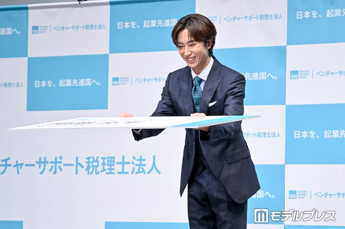 「ベンチャーサポートアンバサダーの阿部亮平と申します」と言いながら特大名刺を前に差し出す阿部亮平(C)モデルプレス