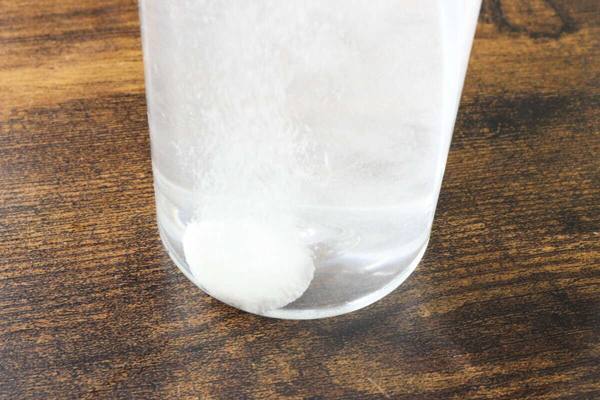 透明なグラスに入った水の中で白い錠剤型クリーナーが泡を出しながら溶けている様子