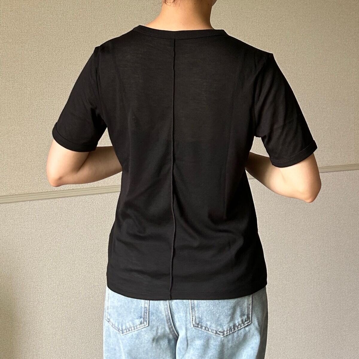 黒いシアーTシャツと薄いブルーのデニムパンツを着用した女性が後ろを向いて立っている