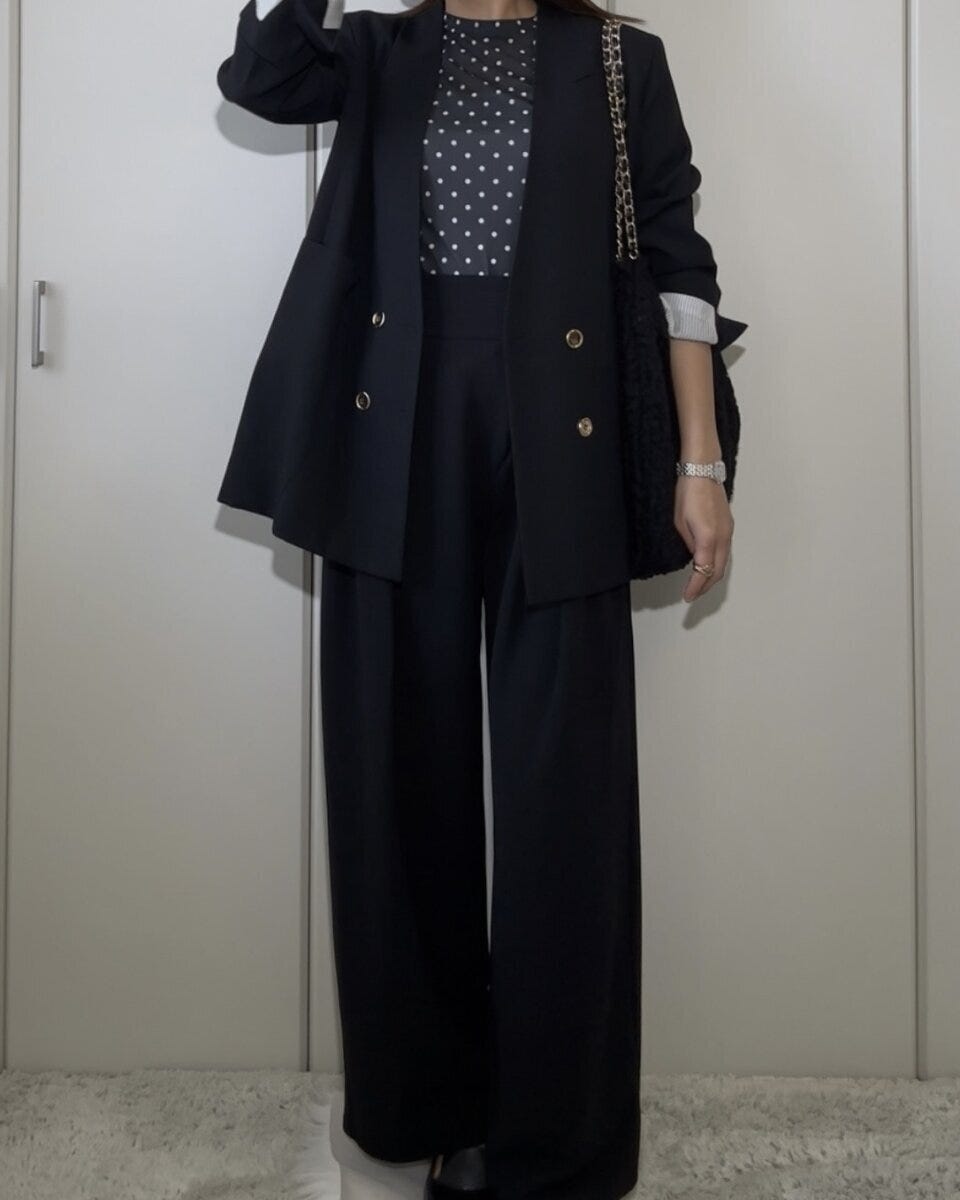 黒いドット柄のシアーTシャツに黒いジャケットとワイドパンツ、黒いバッグを合わせた全身コーデの女性